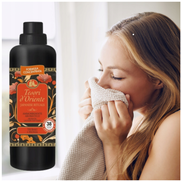 Tesori d'Oriente Japanese Rituals skoncentrowany płyn do płukania tkanin 760ml - czarna butelka z etykietą pomarańczową, obok kobieta wciągająca zapach z szarego materiału.